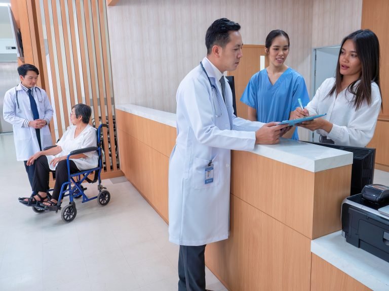 At hospital information counter doctor speaking to administrative crew checking patient status